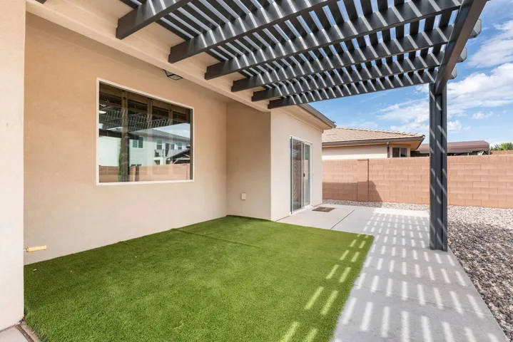 Covered patio featuring a slatted pergola, stucco exterior, artificial turf, concrete hardscaping, and privacy wall