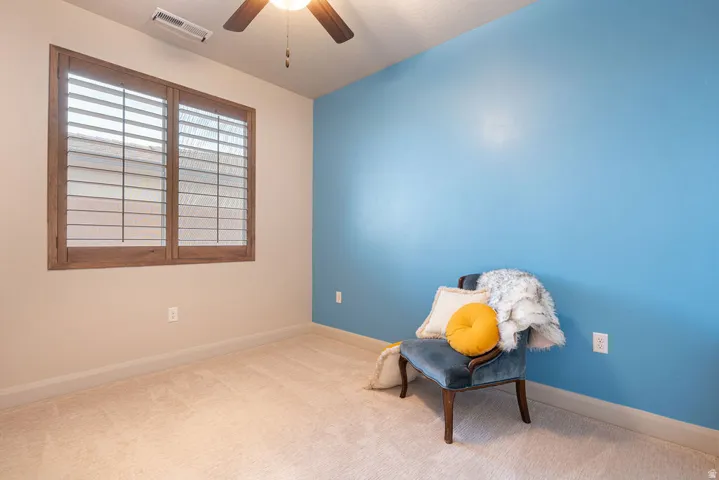 Plush carpeting, wood-finish window shutters, ceiling fan with integrated lighting, and a painted accent wall