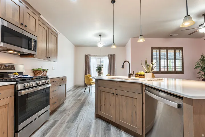 Wood-finish cabinetry, stainless steel appliances, white countertops, wood-finish flooring, and pendant lighting