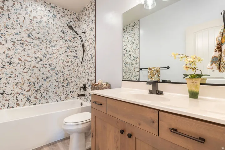 Terrazzo-style shower surround, white bathtub, wood-finish vanity with countertop, rectangular undermount sink, and matte black fixtures