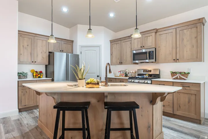 Kitchen featuring wood-finish cabinetry, stainless steel appliances, a center island with seating, pendant lighting, and light-toned countertops