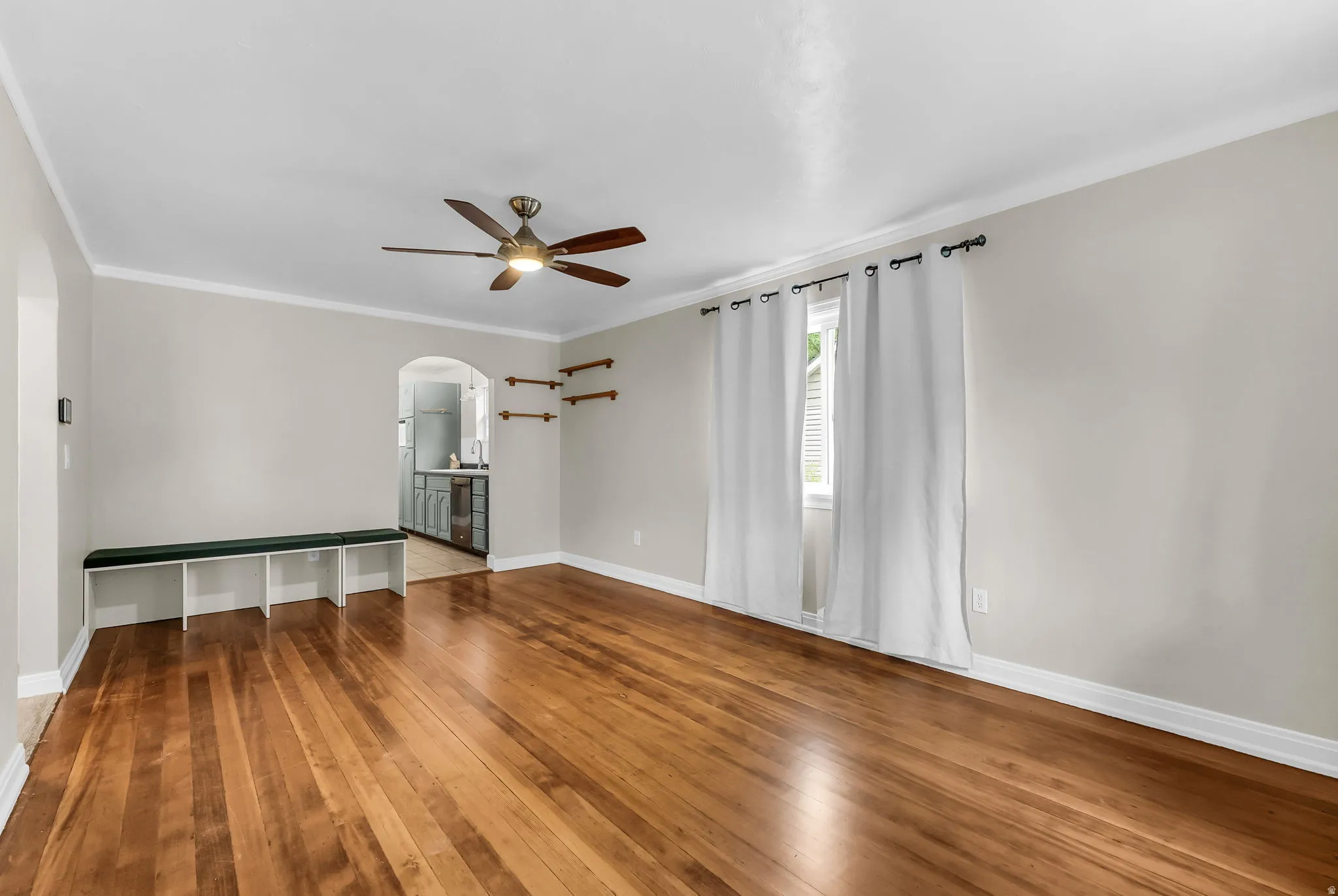 Hardwood flooring throughout, arched doorway, ceiling fan, and window with natural light