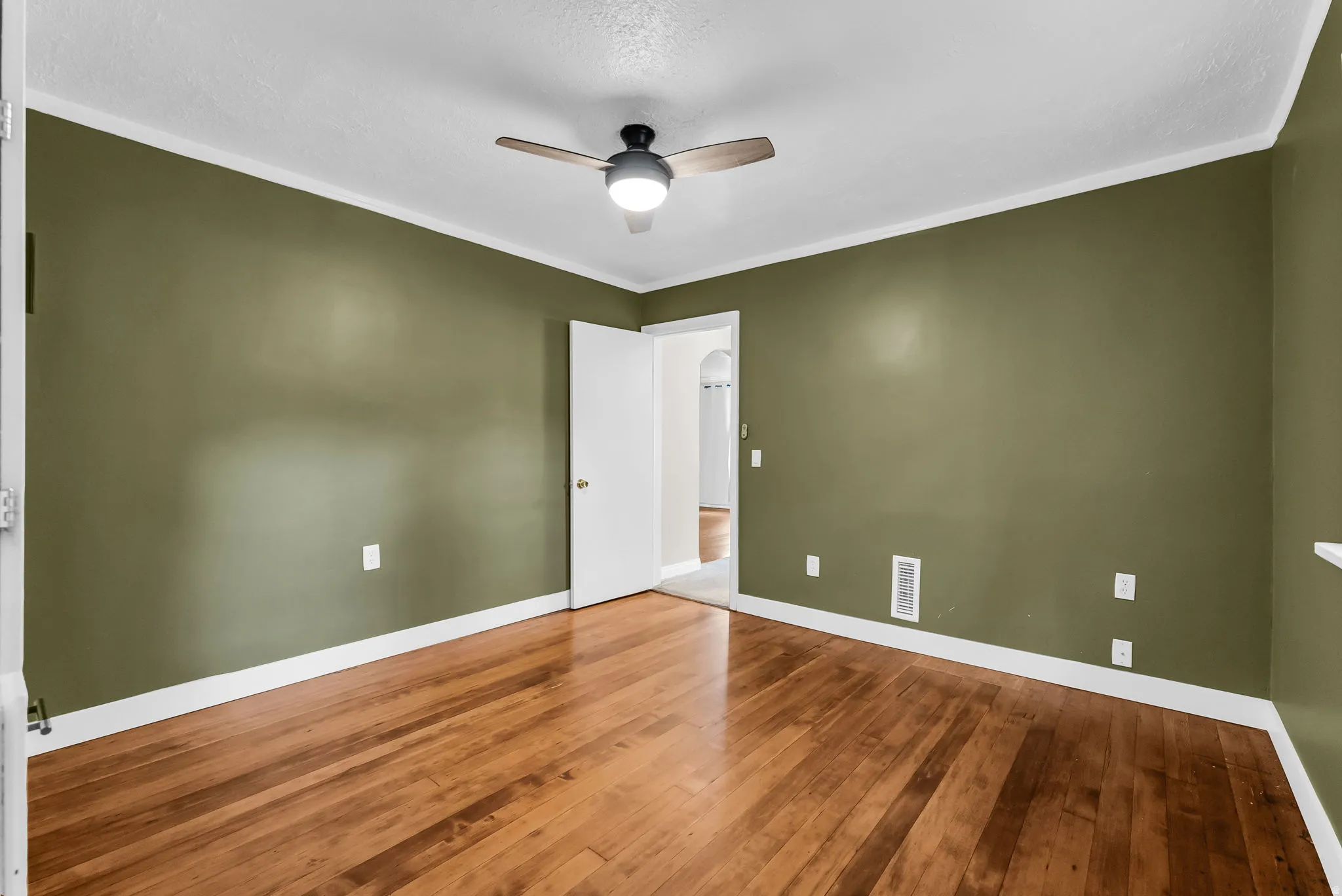 Wood-finish flooring with white trim, wall-mounted ceiling fan with integrated lighting, and solid interior doors