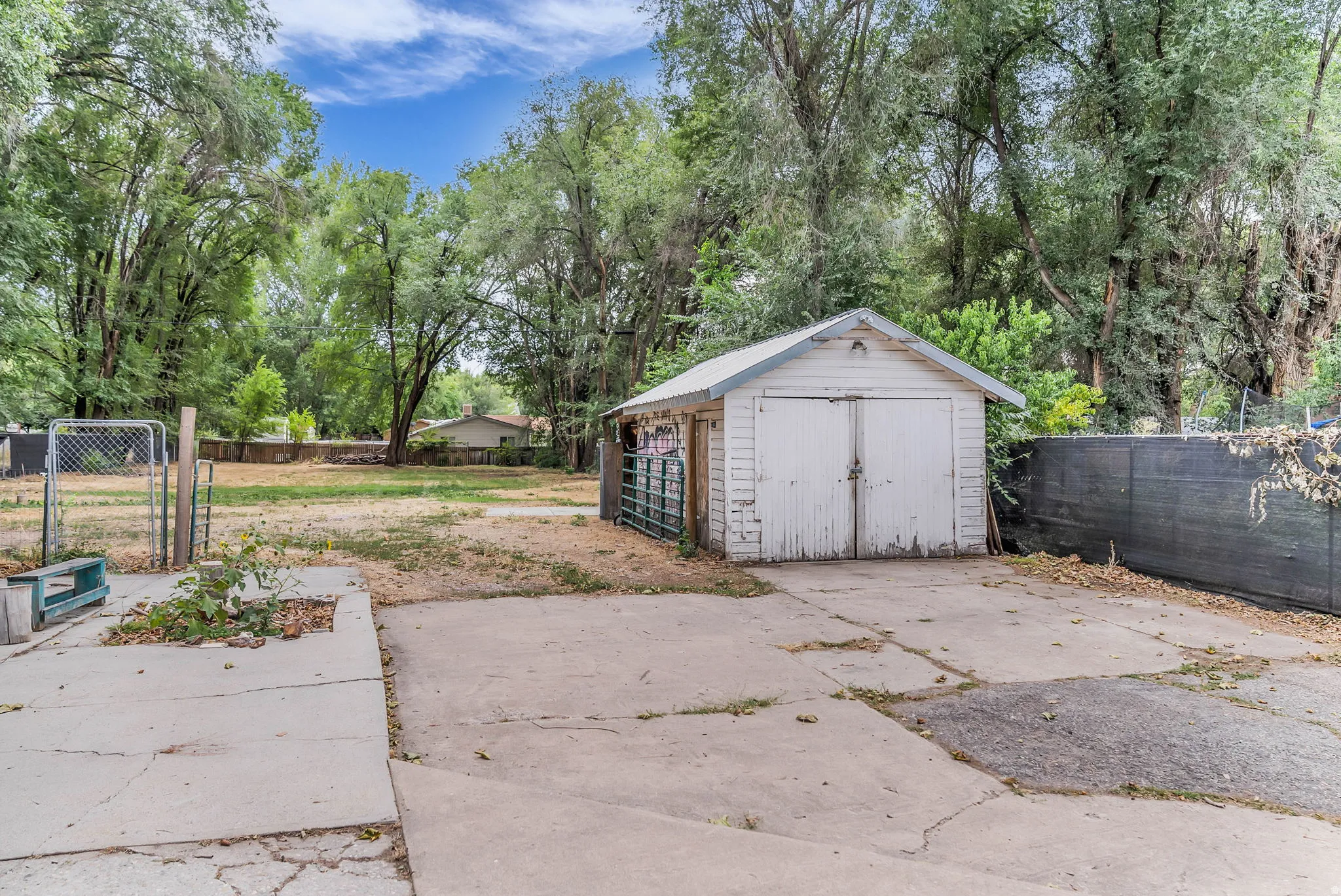 Detached outbuilding with double-door entry, concrete pad, chain-link gate, and perimeter fencing