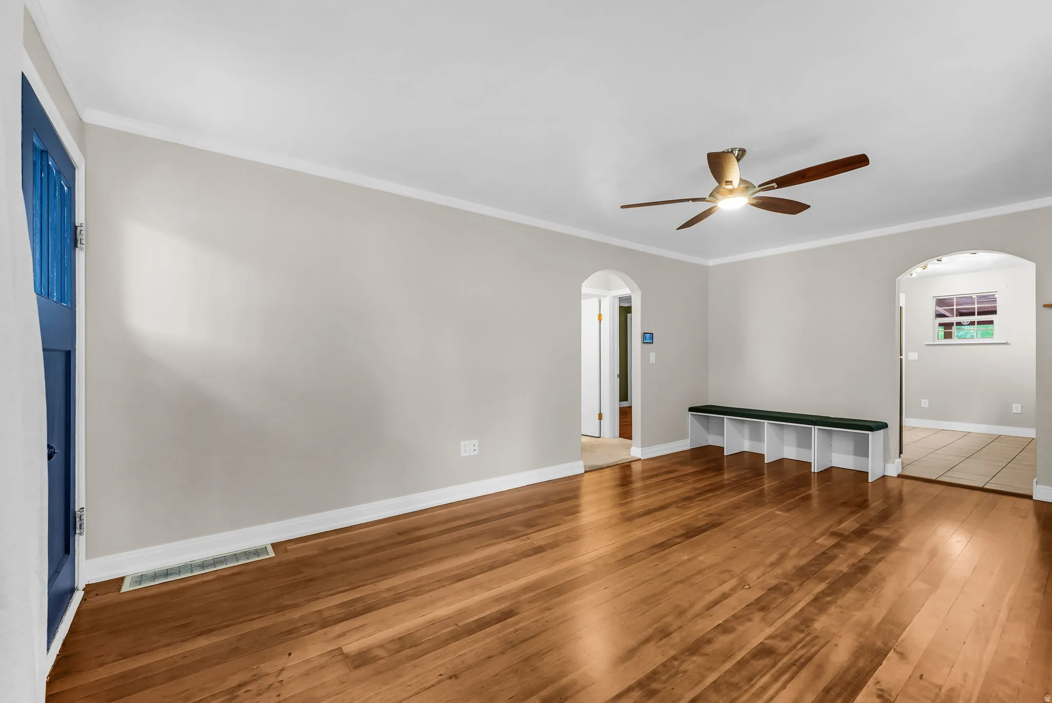 Wood-finish flooring, white crown molding, arched doorways, and a ceiling fan with integrated lighting