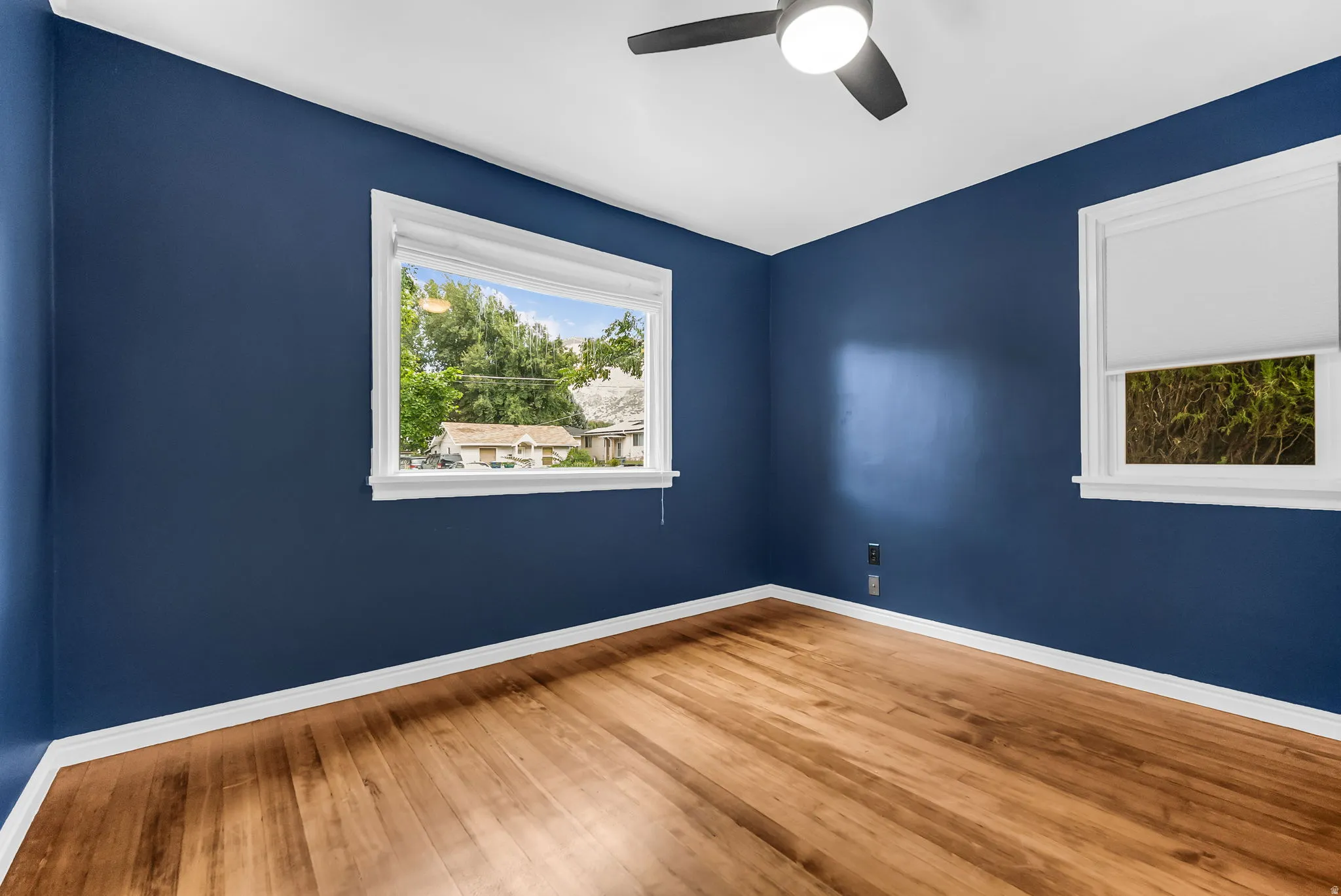 Hardwood-style flooring, white trim, ceiling fan with integrated lighting, and multiple windows