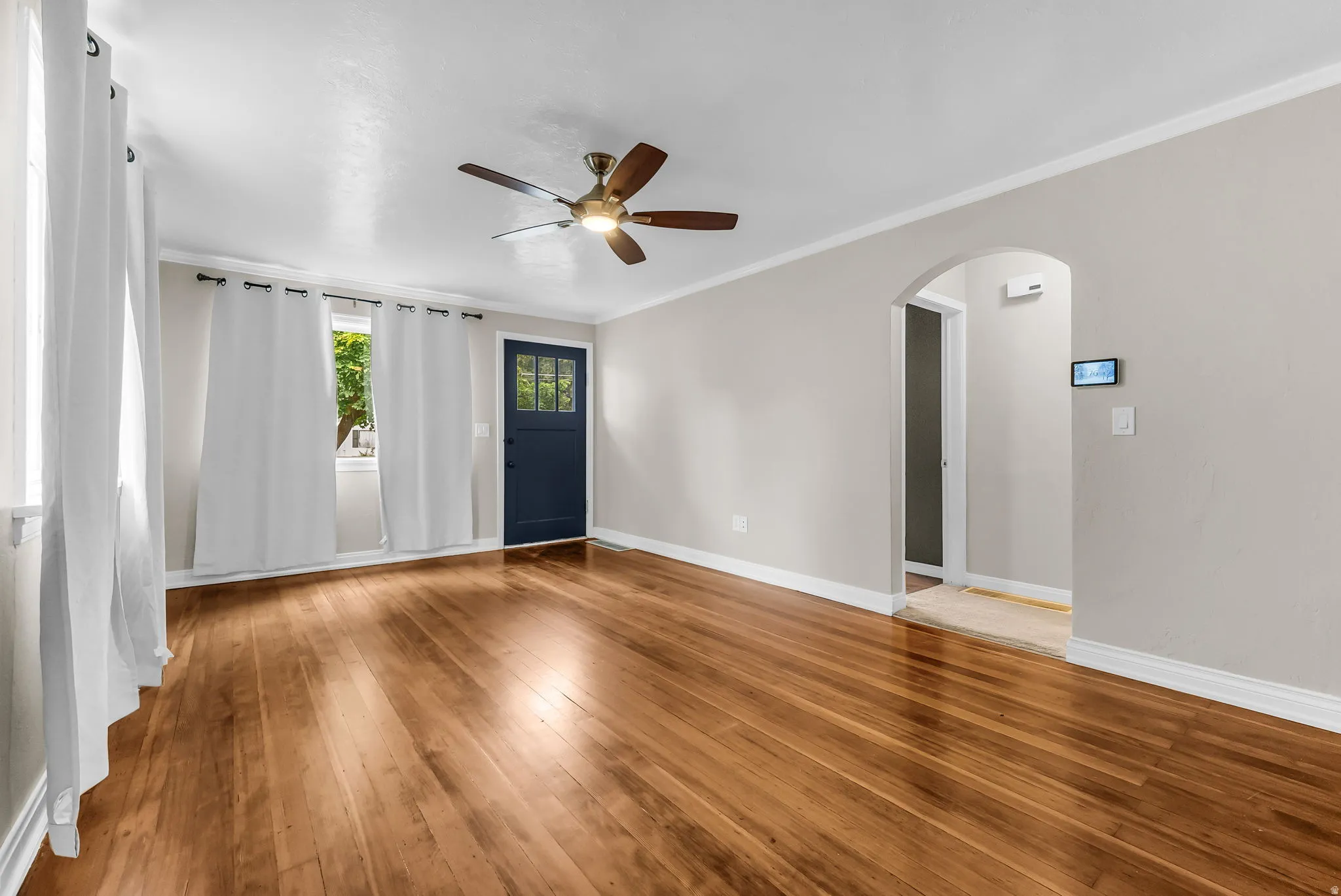 Hardwood flooring throughout, featuring a ceiling fan with integrated lighting, an arched doorway, and a dark-paneled door with glass inserts