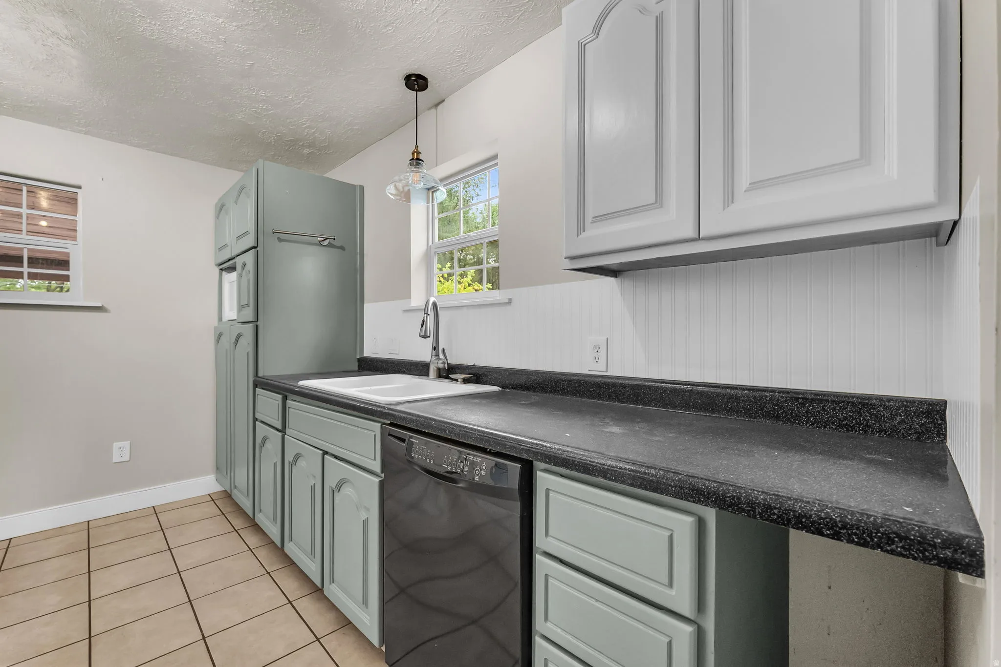 Kitchen featuring light blue lower cabinetry, white upper cabinetry, dark countertops, a white sink with a chrome faucet, and white beadboard backsplash