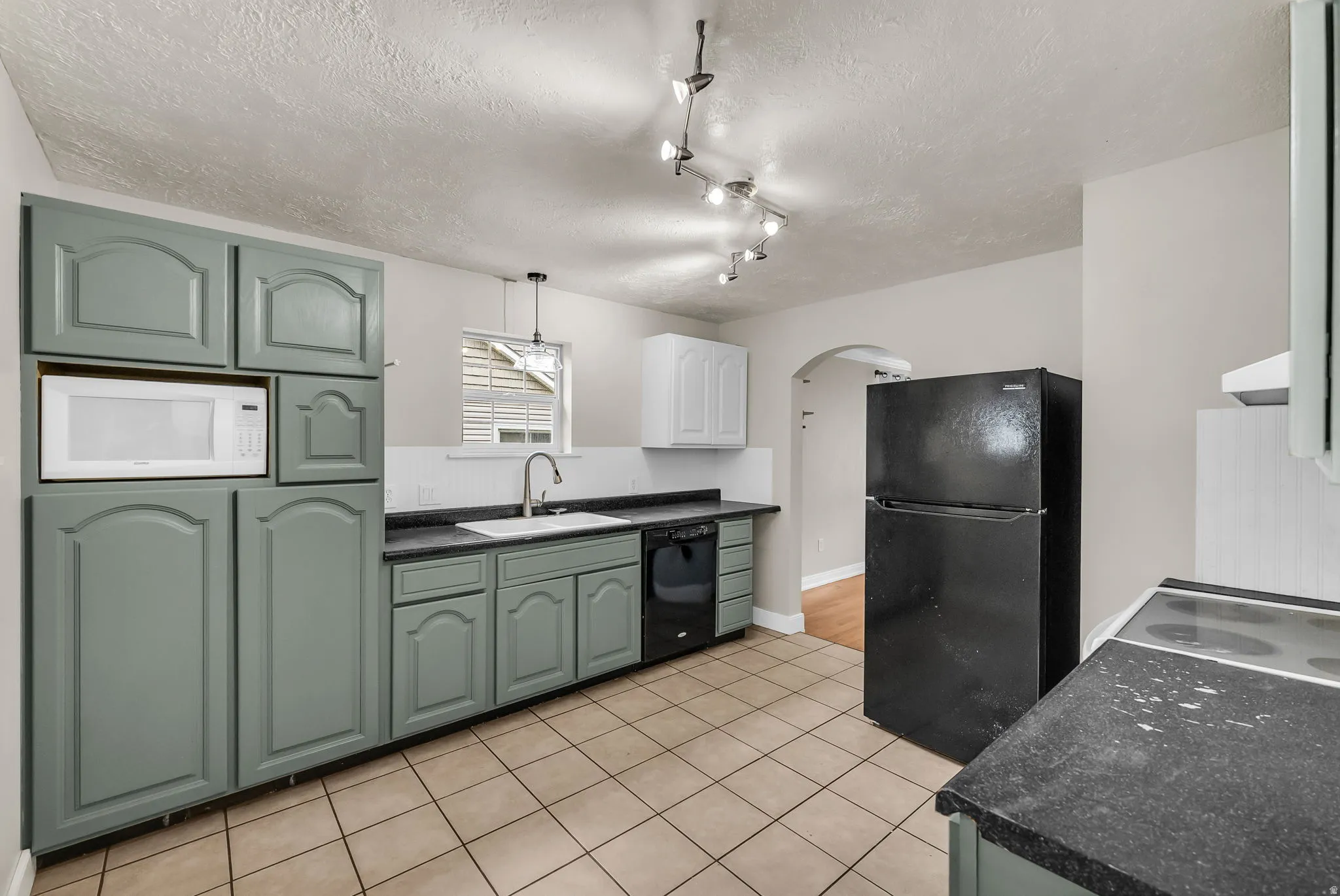 Kitchen featuring ample cabinetry, tile flooring, built-in microwave, dark countertops, and a window above the sink