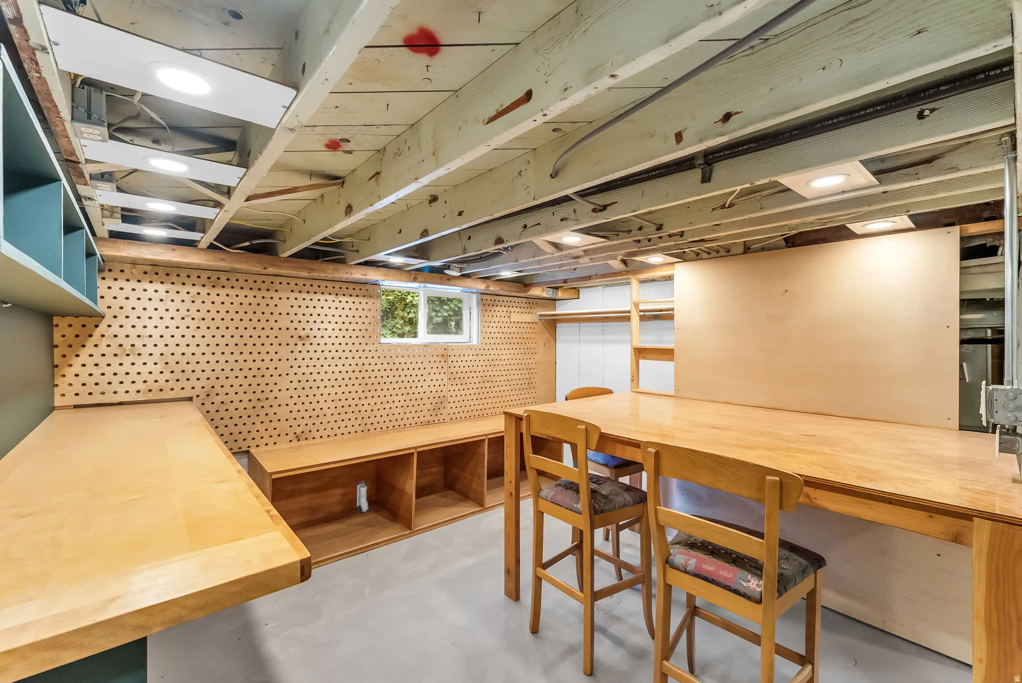 Exposed ceiling joists with recessed lighting, pegboard wall, built-in shelving, and a large wooden workbench