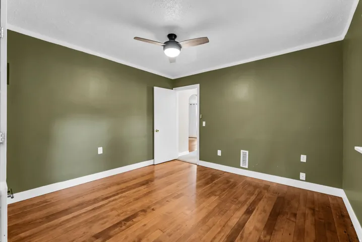Wood-finish flooring with white trim, wall-mounted ceiling fan with integrated lighting, and solid interior doors
