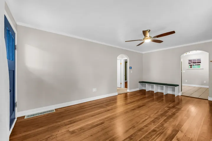 Wood-finish flooring, white crown molding, arched doorways, and a ceiling fan with integrated lighting