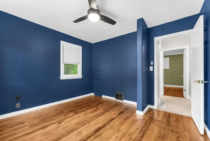 Wood-finish flooring with white trim, a ceiling fan with integrated lighting, and a white-framed window