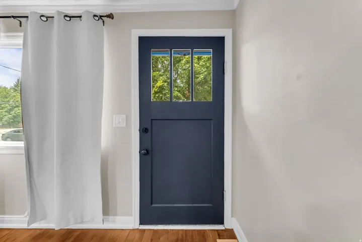 Navy panel door with upper glass inserts, wood-finish flooring, and light neutral wall paint