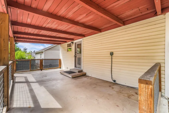 Covered outdoor patio with a concrete floor, wood-plank ceiling, and wood-framed railings with mesh infill