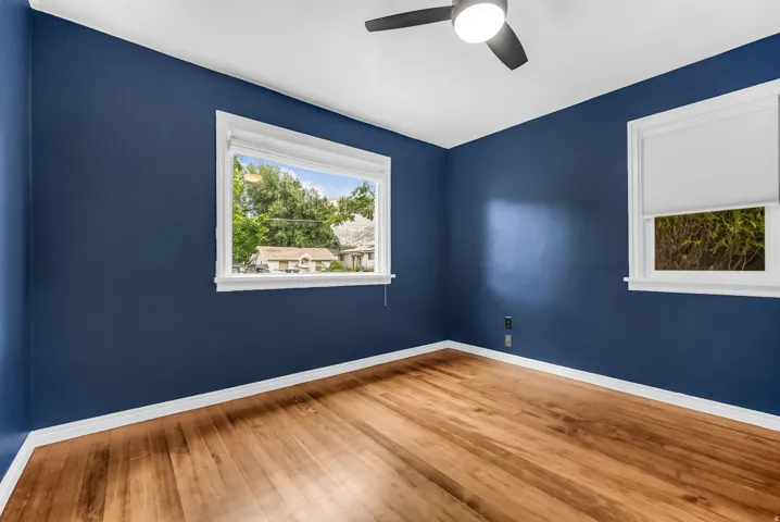 Hardwood-style flooring, white trim, ceiling fan with integrated lighting, and multiple windows