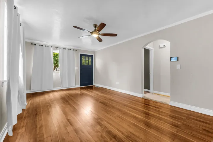 Hardwood flooring throughout, featuring a ceiling fan with integrated lighting, an arched doorway, and a dark-paneled door with glass inserts