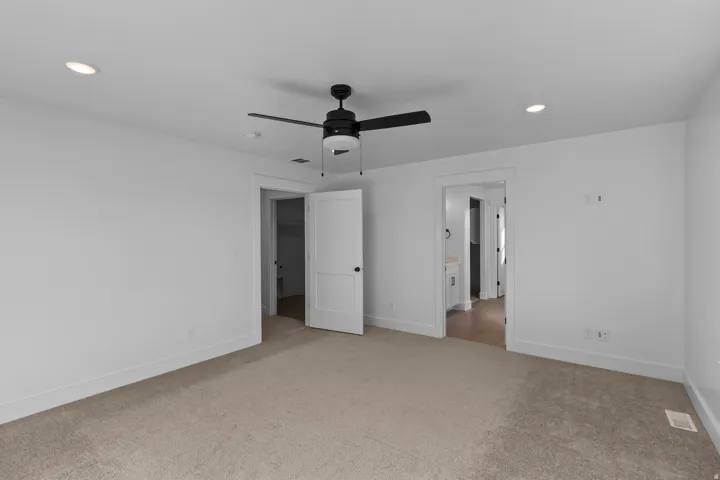 Neutral tone carpeting, recessed ceiling lighting, a matte black ceiling fan, and white interior doors