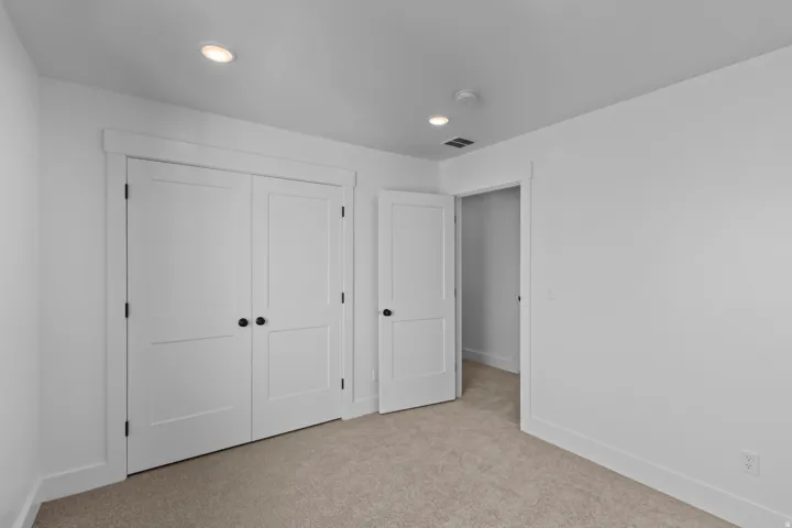Neutral wall color, recessed ceiling lighting, two-panel interior doors with matte black hardware, and carpet flooring
