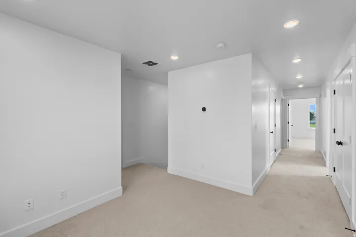Recessed lighting illuminates the neutral-toned carpeting and white walls, complemented by white trim and black door hardware