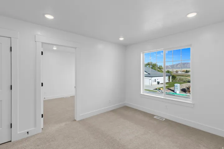 Recessed lighting, neutral carpeting, white interior doors, and a large window with grid panes