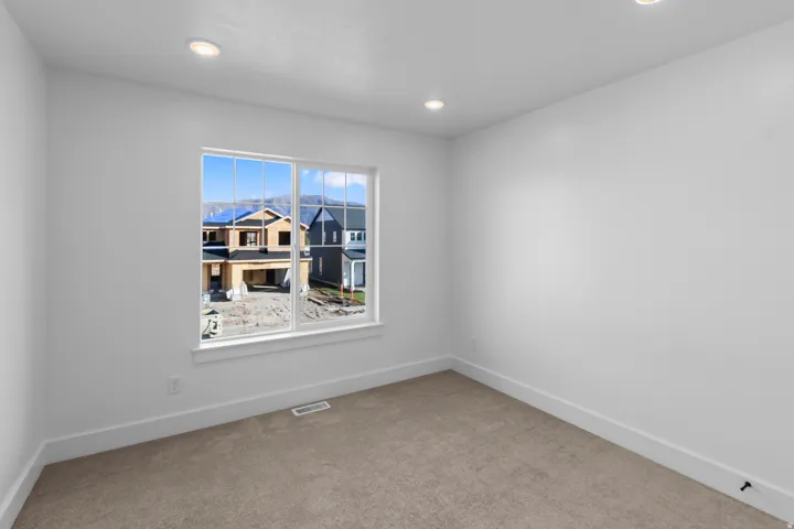 Recessed ceiling lighting, white painted walls, window with white trim, and neutral carpeting