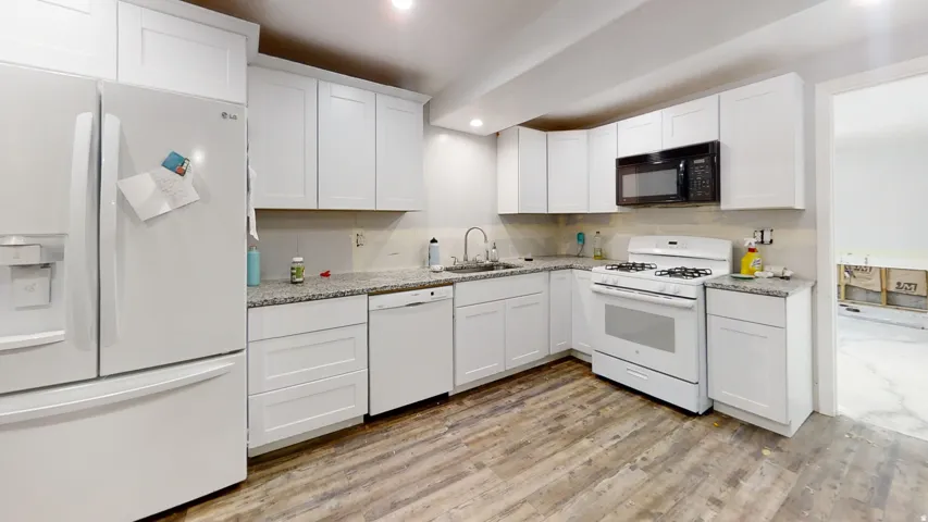 White cabinetry, granite-finish countertops, stainless steel sink with gooseneck faucet, white gas range, and wood-finish flooring