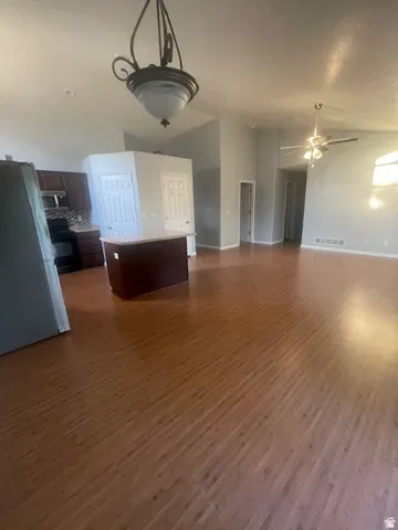 Expansive open-concept living area featuring wood-finish flooring, vaulted ceilings, and a kitchen island with a light-toned countertop