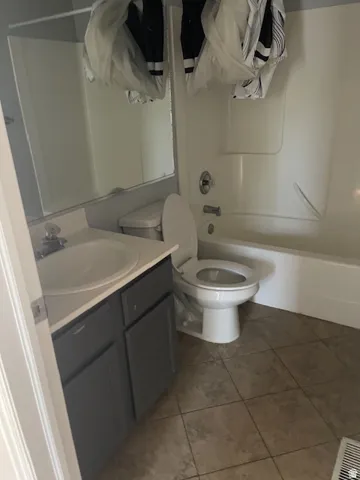 Bathroom featuring a white bathtub, toilet, vanity with a white basin sink, grey cabinetry, and tile flooring