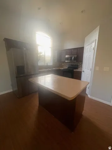 Kitchen featuring wood-finish flooring, dark wood cabinetry, a central island, stainless steel refrigerator, and a curved arch window