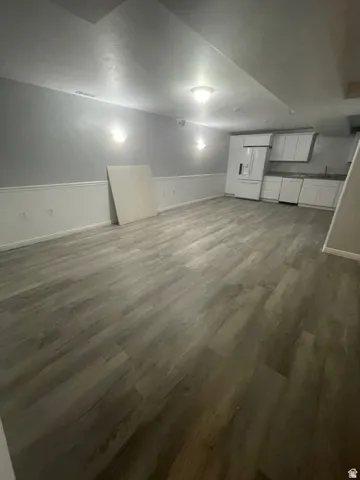 Wood-finish flooring, white wainscoting, integrated kitchen area with white cabinetry, white refrigerator, and modern ceiling lighting