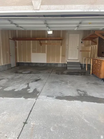 Concrete flooring garage with built-in wooden shelving, a white entry door, and integrated overhead lighting