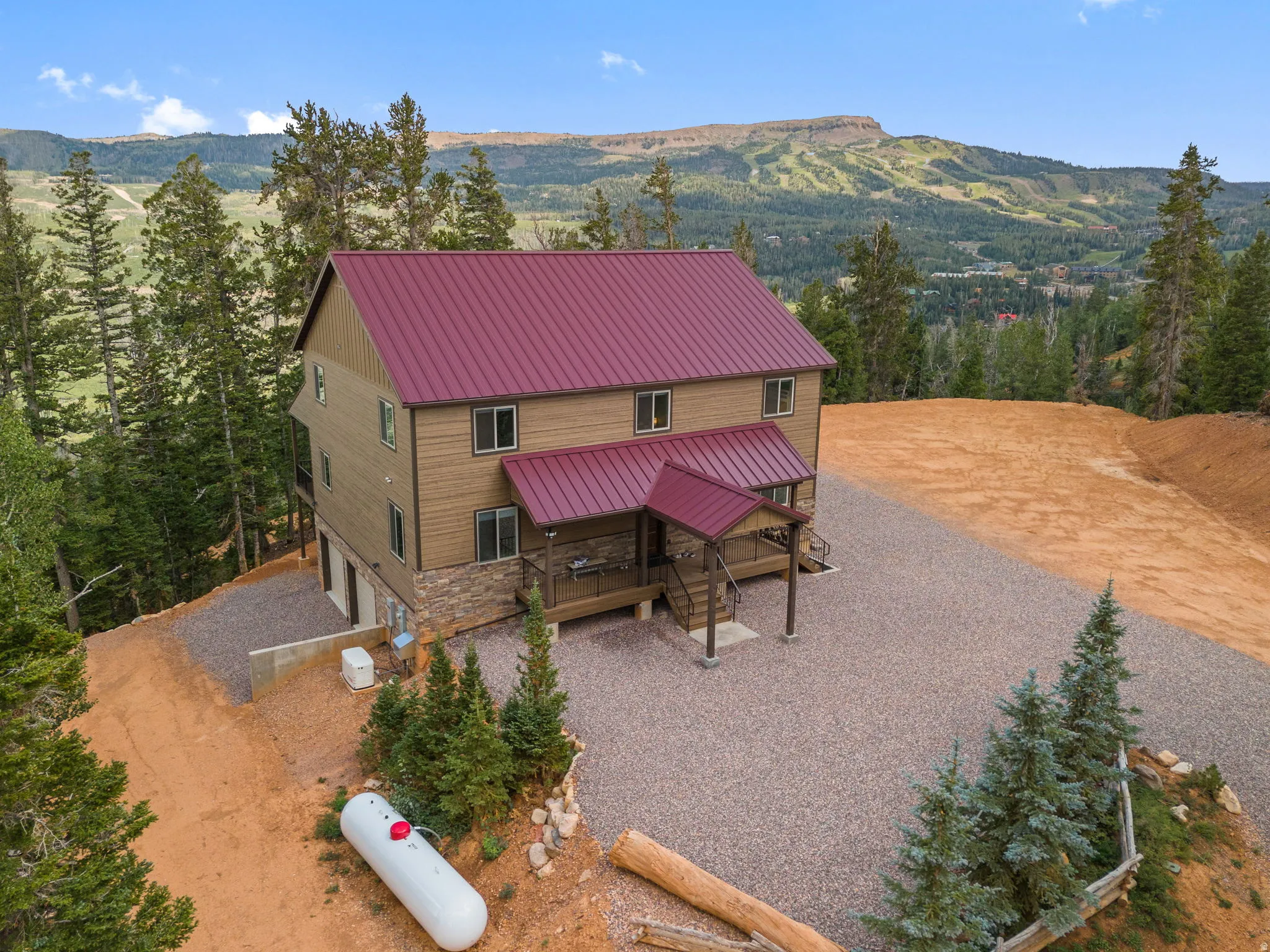 Mountain backdrop with a multi-level residence featuring a red metal roof, stone facade accents, and a covered porch entry