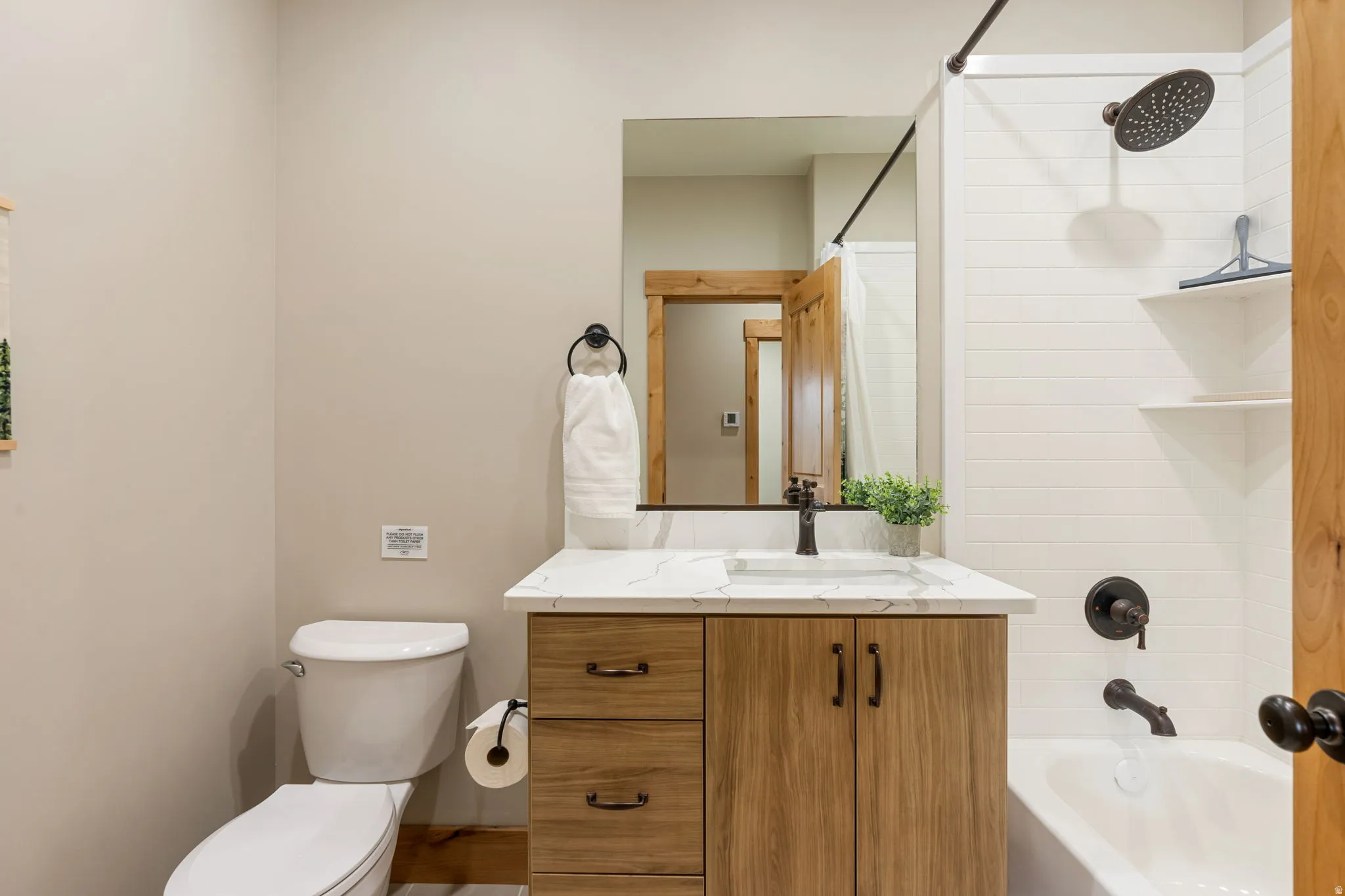 Bathroom featuring a wood-finish vanity with a white countertop, a built-in tub, white horizontal wall paneling in the shower, and dark bronze fixtures