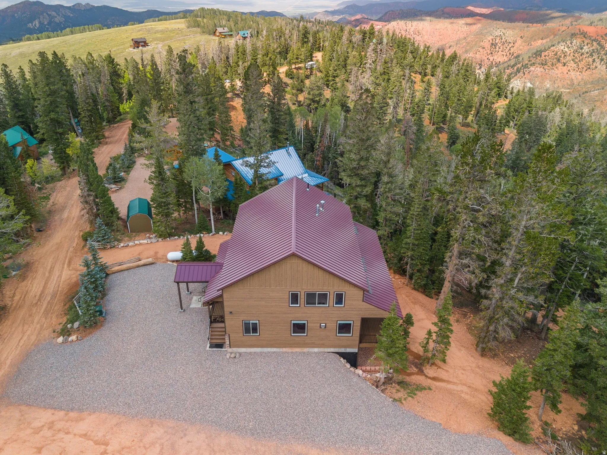 Expansive gravel driveway, wood-sided exterior, burgundy metal roof, covered entry, and surrounding mature trees
