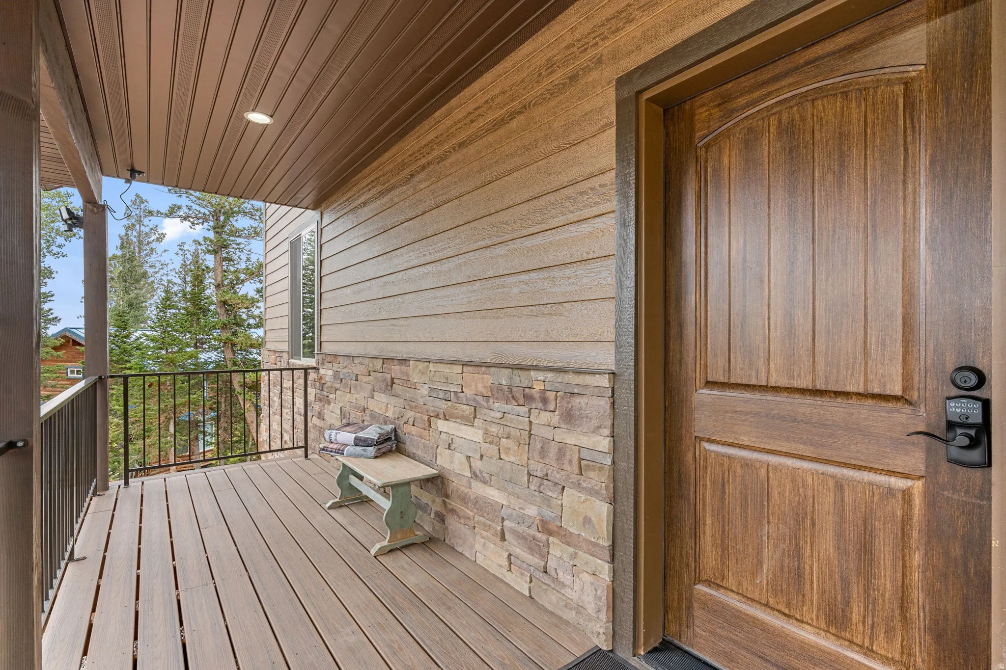 Covered front porch featuring wood-finish siding, stone veneer accents, and wood-finish composite decking