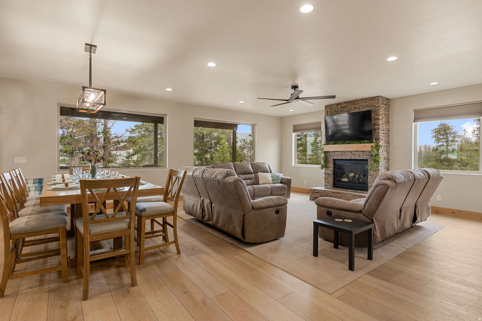 Open concept living and dining area featuring wood-finish flooring, a stone-clad fireplace with a mantel, and recessed lighting