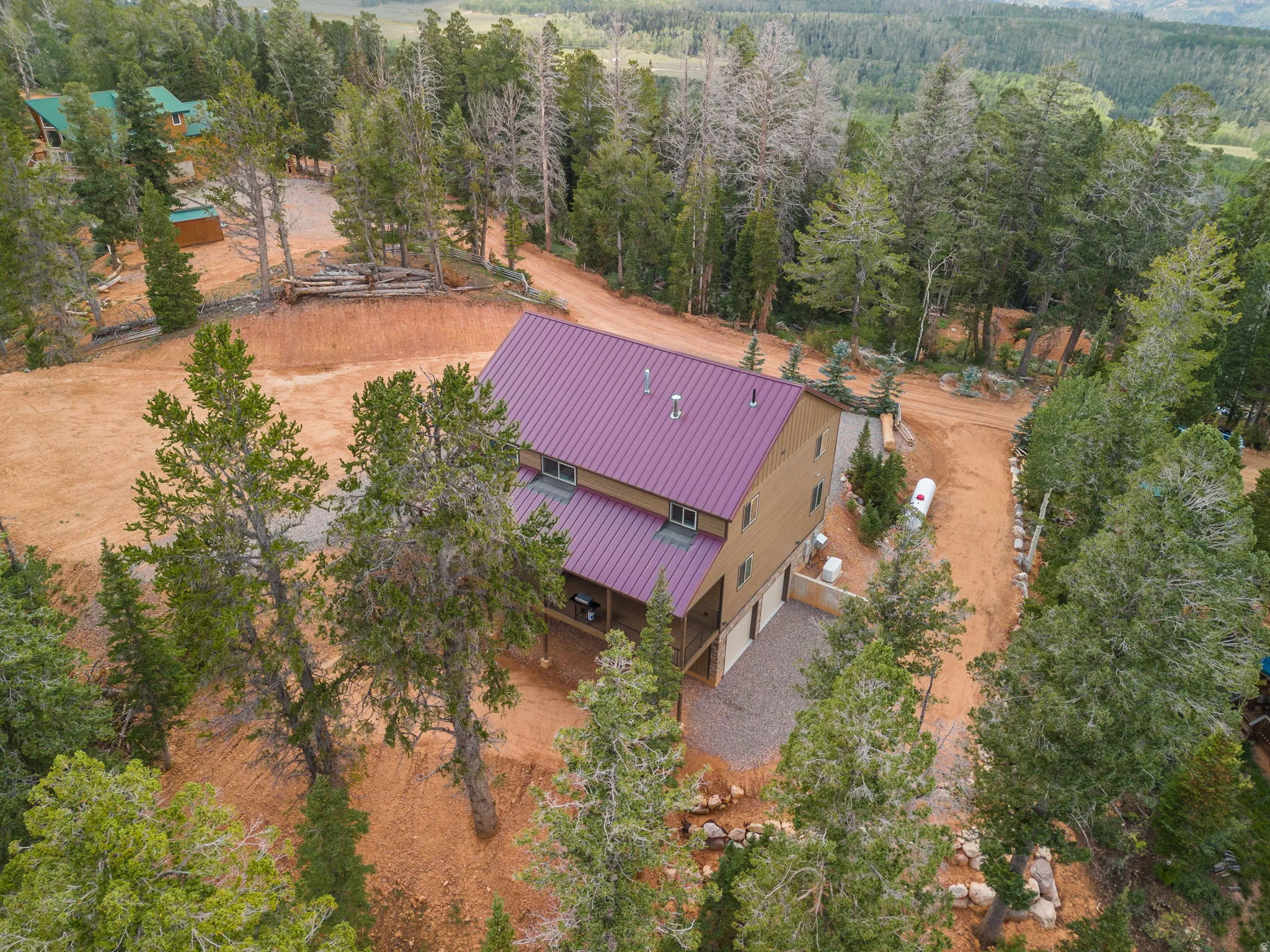 Two-story residence with a purple metal roof, tan siding, and a gravel driveway