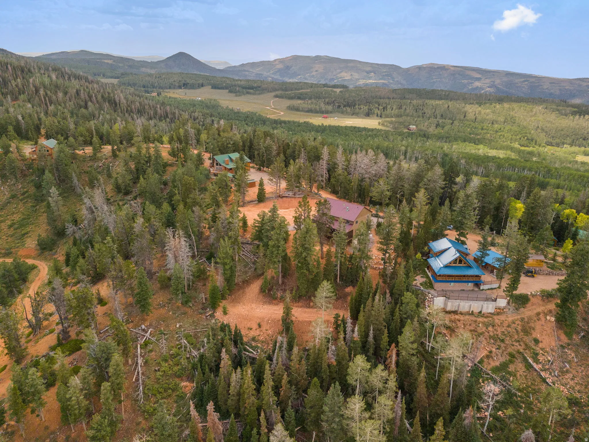 Mountainous landscape featuring multiple properties, dense evergreen tree coverage, and a distant valley