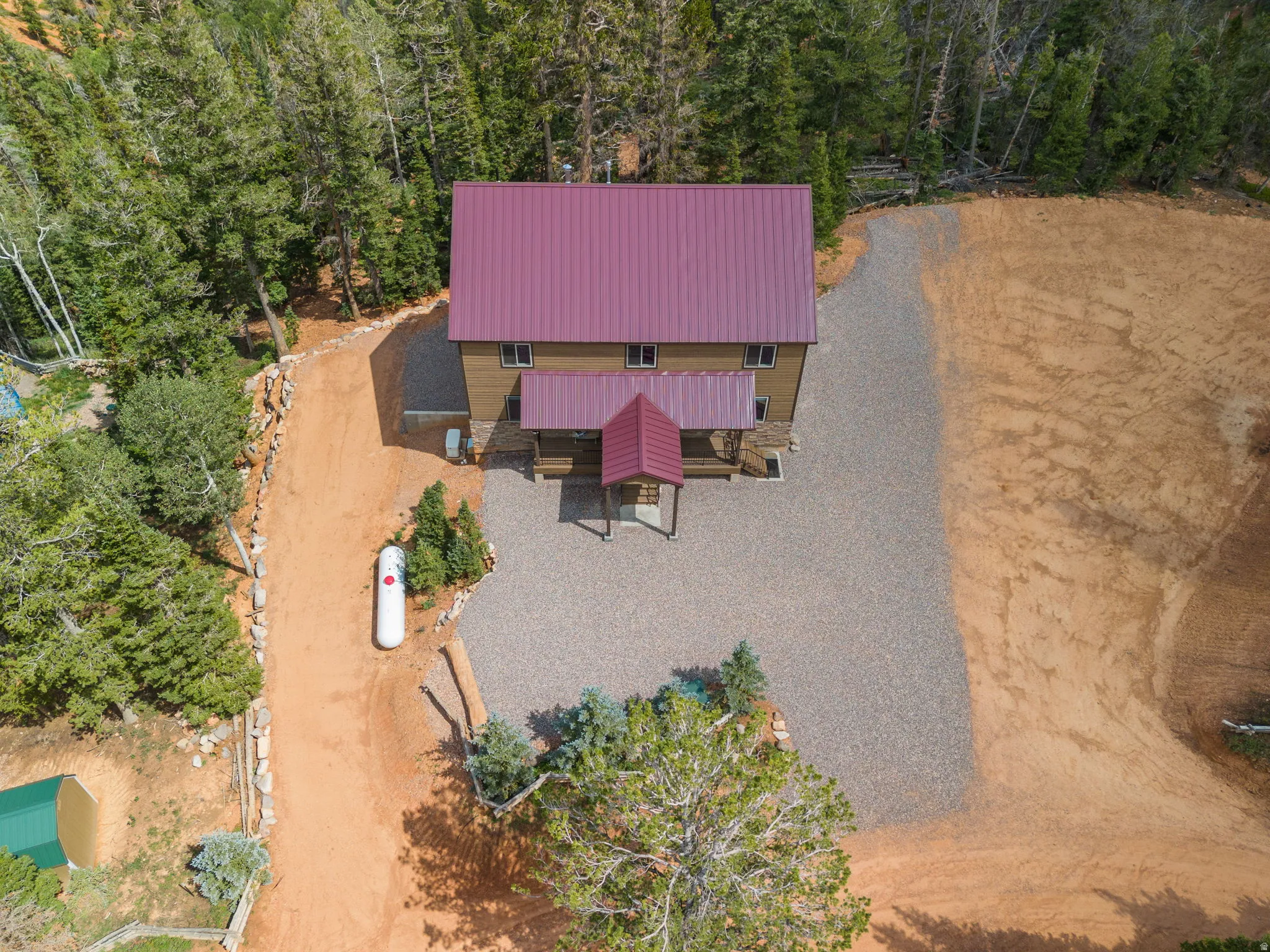 Two-story property with a red metal roof, surrounded by mature trees