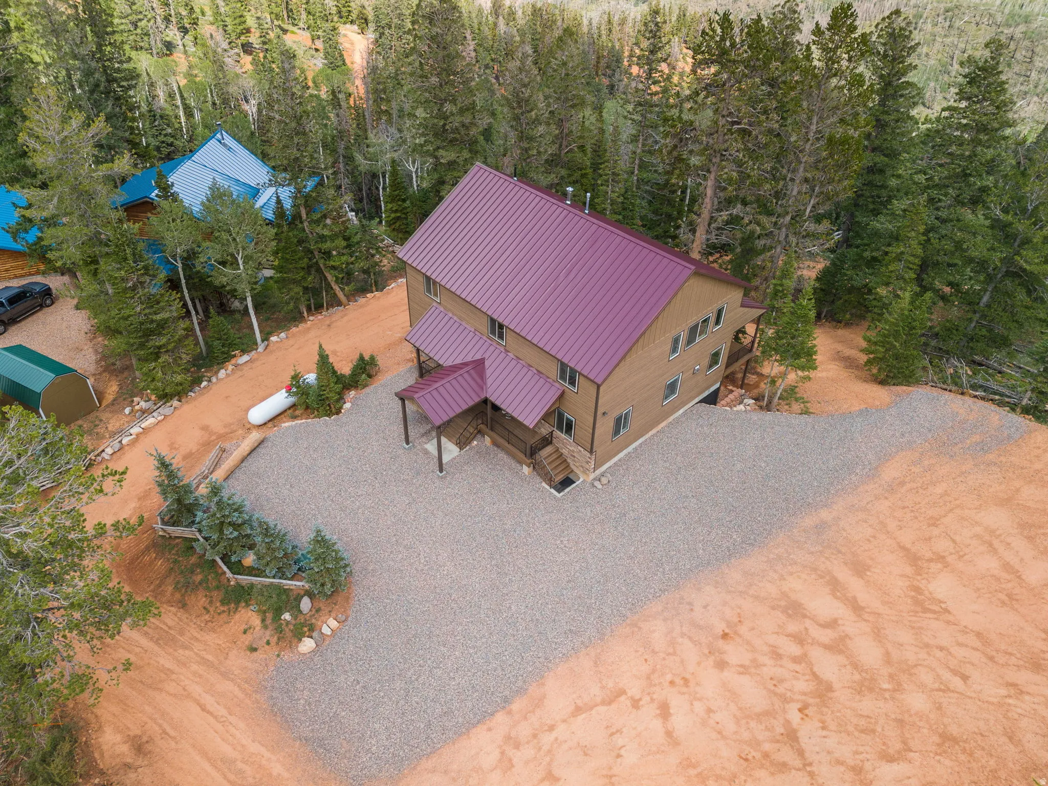 Multi-story residence featuring a maroon metal roof, light brown siding, and a covered entry porch