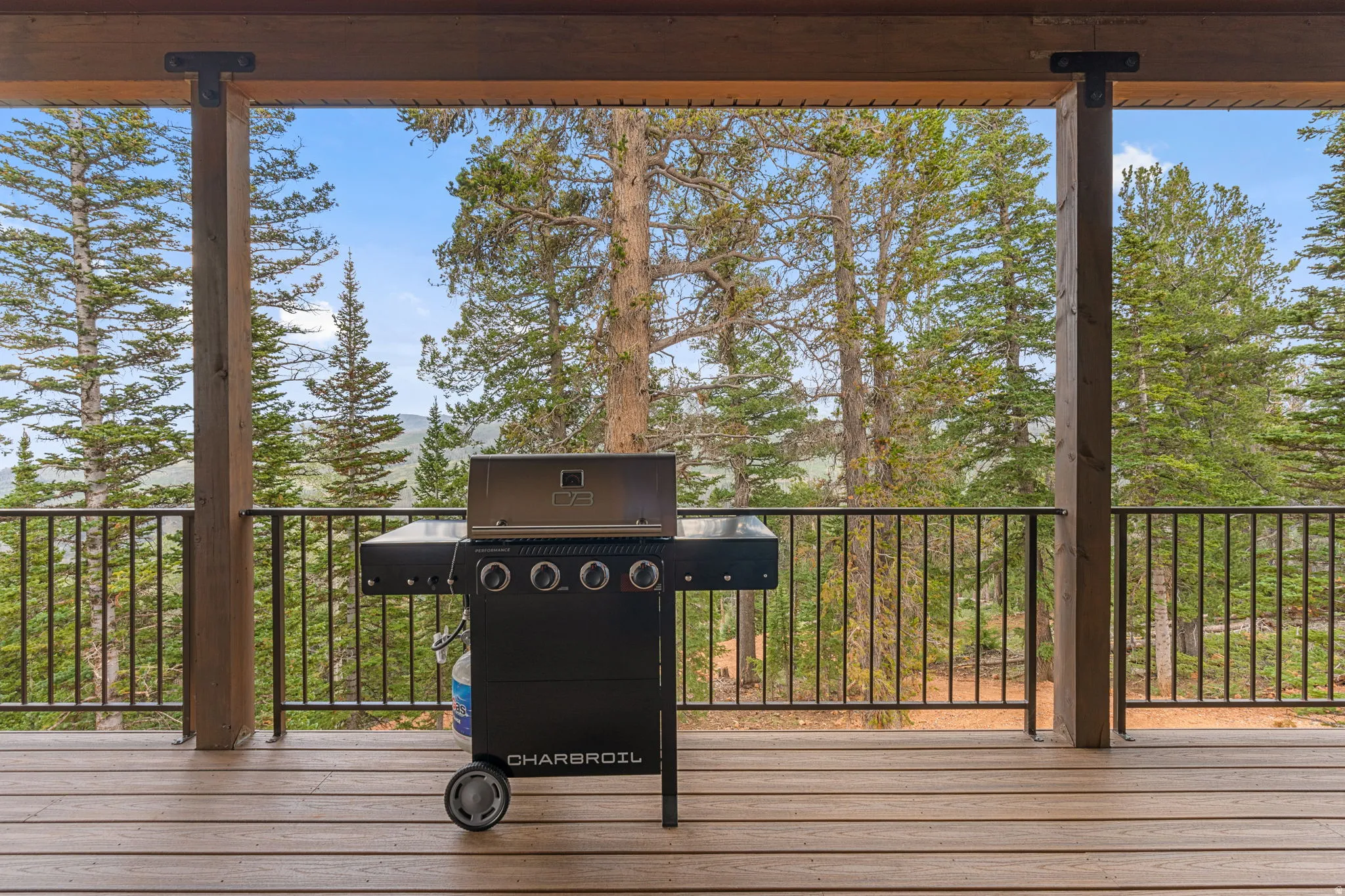 Covered outdoor deck with wood-finish flooring, black metal railing, and exposed wood beams