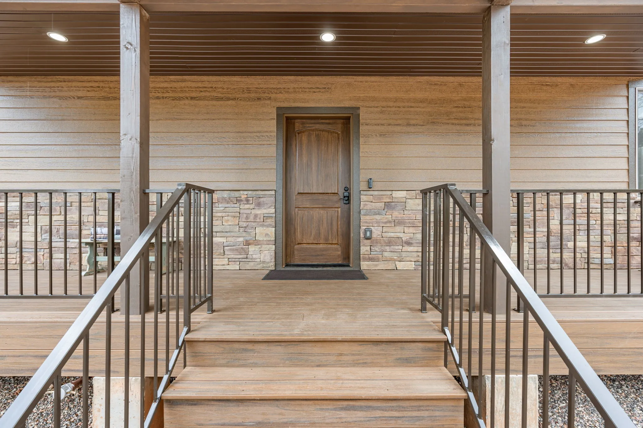 Front porch with wood-finish decking, dark metal railings, and stone veneer accents