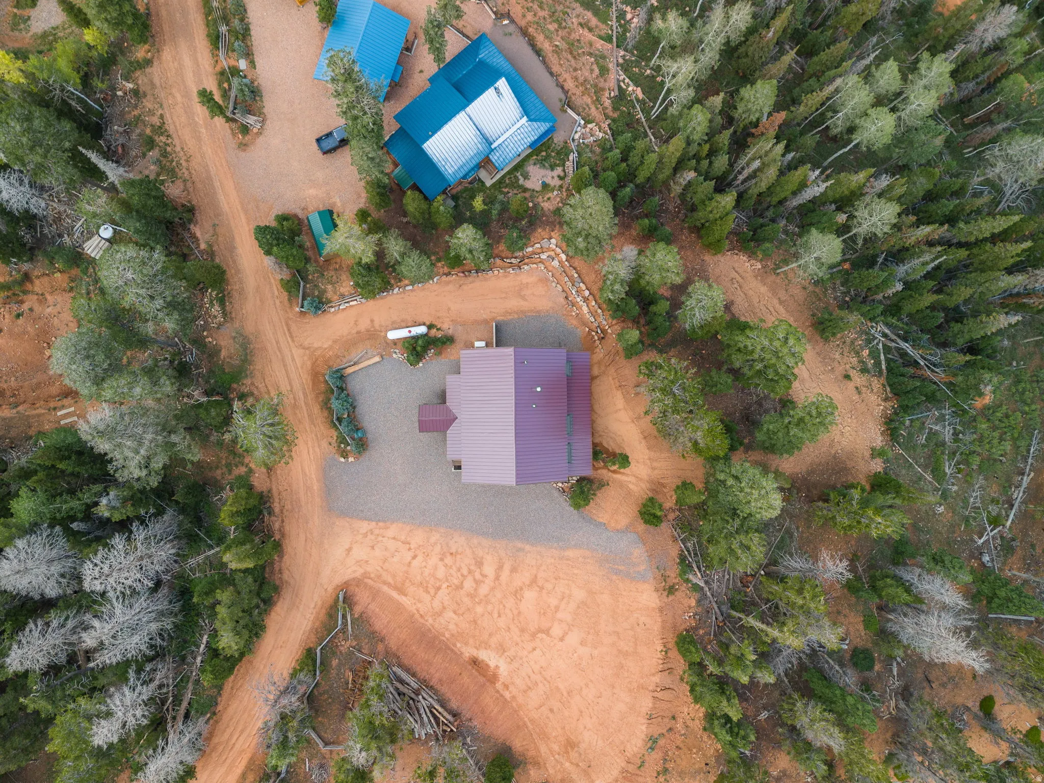 Property featuring two residences with metal roofs, surrounded by dense evergreen and deciduous trees, accessed by a network of dirt roads