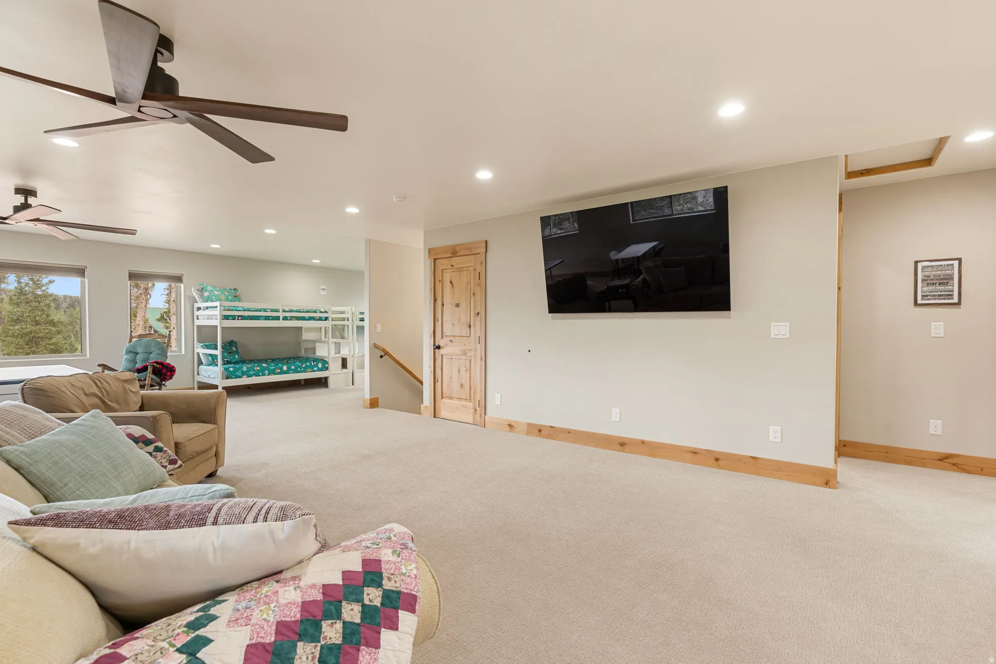 Recessed lighting illuminates this carpeted space featuring a ceiling fan, light wood trim, and a natural wood-finish door
