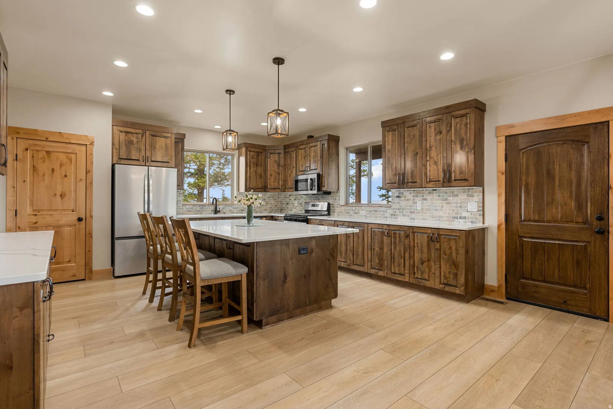 Spacious kitchen featuring wood-finish cabinetry, a large center island with seating, stainless steel appliances, a tile backsplash, and recessed lighting