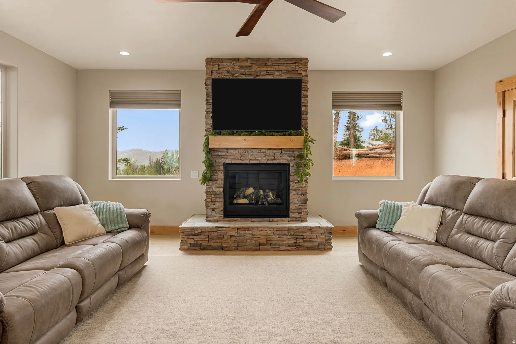 Stacked stone fireplace with a wood mantle and hearth, recessed lighting, and a ceiling fan