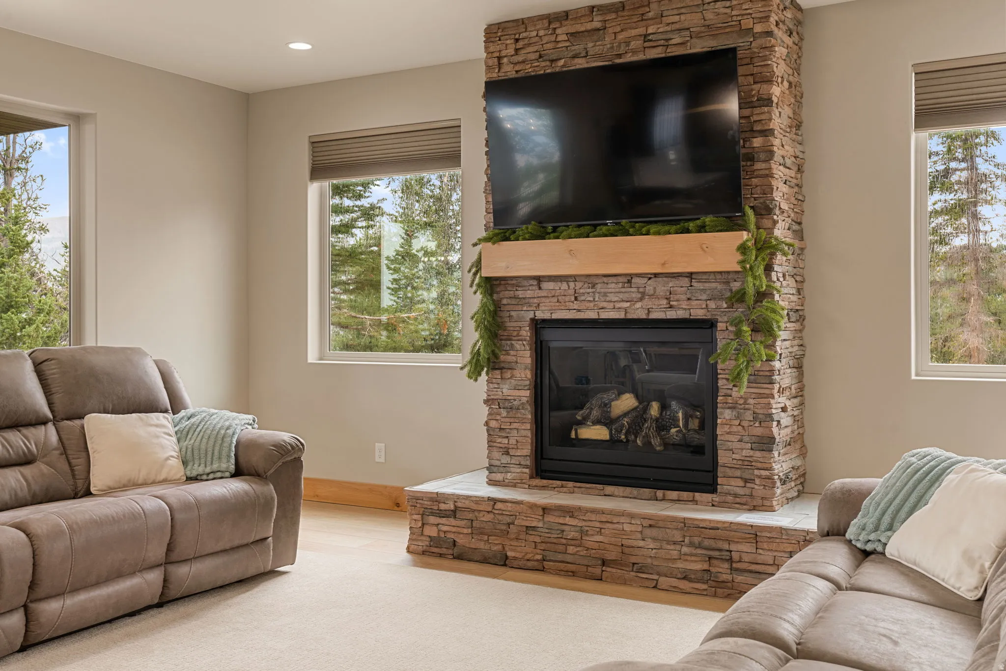 Carpeted living area featuring a stone-clad fireplace with a wood mantel, recessed lighting, and multiple windows