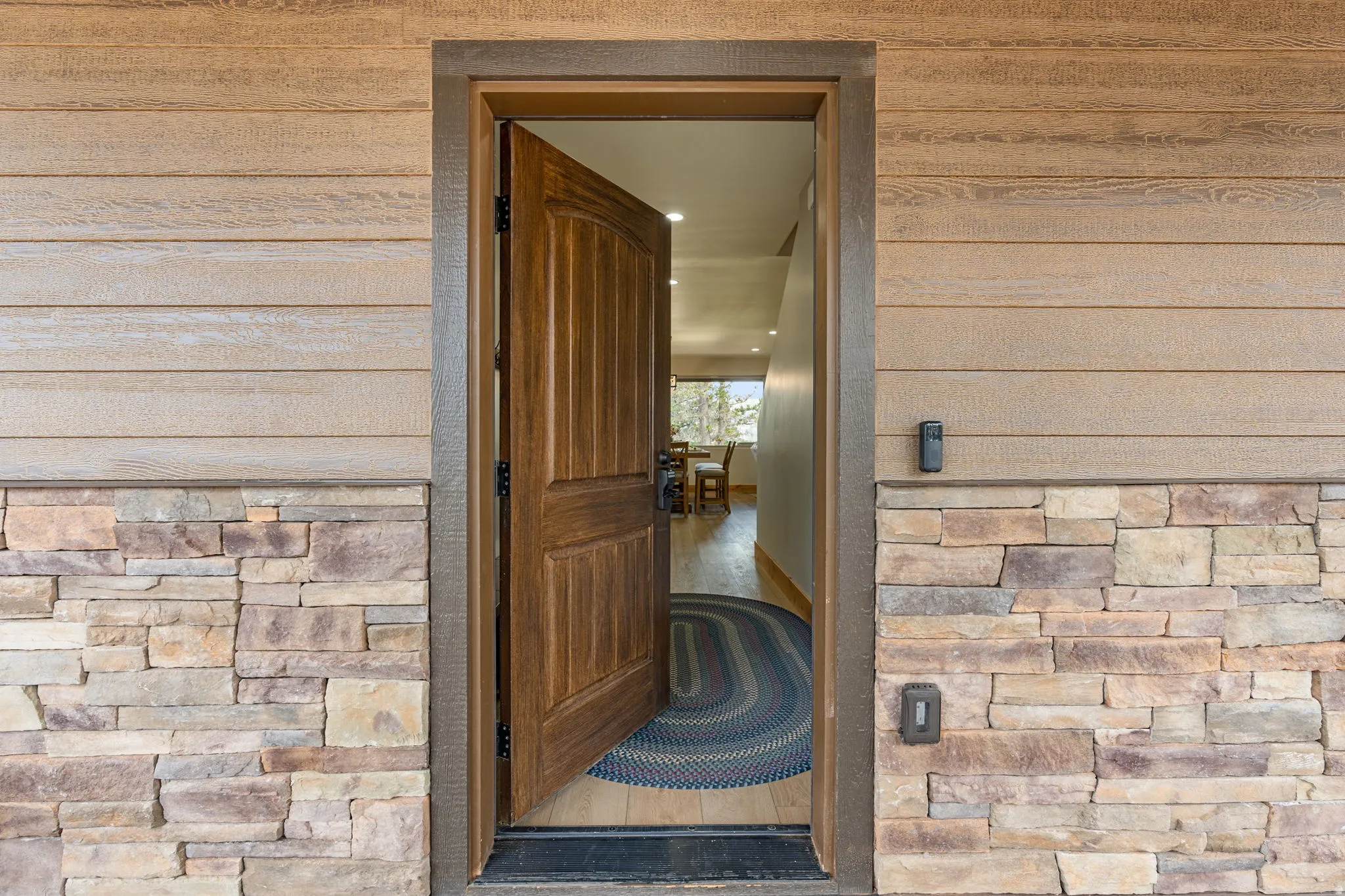Wood-finish siding with stone veneer accents, solid wood entry door, and wood-finish flooring