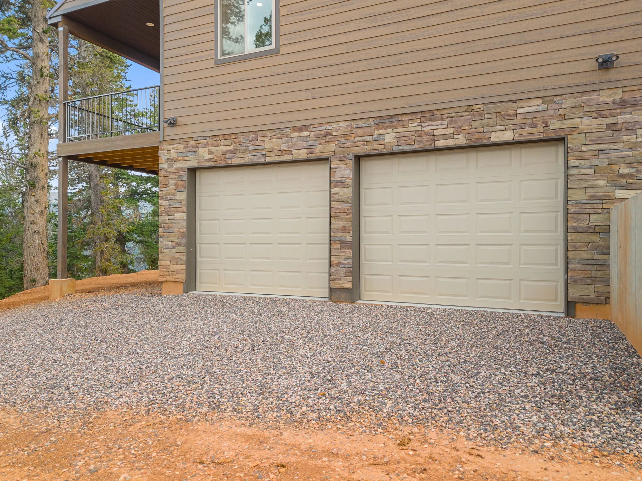 Two-car garage with panel doors, stone veneer accents, horizontal siding, and a gravel driveway